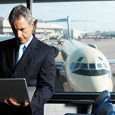 businessman at airport terminal using laptop with view of airplane through window